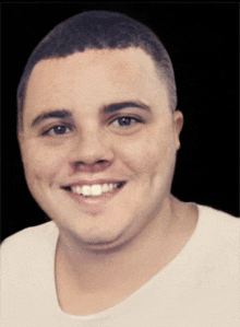 a man with a shaved head is smiling and wearing a white shirt