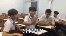 a group of young men are sitting at desks in a classroom and one of them is saying " stop "