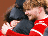 a man in a red expedia jersey hugging another man