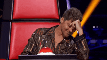 a man with curly hair is sitting in a chair with his hand on his face .