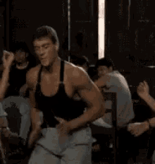 a man in a black tank top and white pants is dancing in a room with other people .