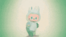 a red stuffed animal in a bunny costume is standing on a pink background .