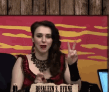 a woman giving a peace sign in front of a sign that says rosaleen s. byrne on it
