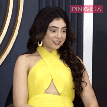 a woman in a yellow dress is sitting in front of a pinkvilla banner