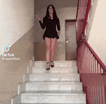a woman in a black dress is walking up a set of stairs with a red railing
