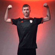 a man in an adidas shirt flexes his muscles in front of a red background