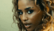 a close up of a woman 's face with curly hair and earrings looking at the camera .