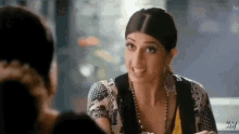 a woman is sitting at a table talking to another woman while wearing a necklace .