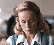 a woman with blonde hair is wearing a white shirt and a blue vest .