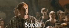 a man with a crown on his head is standing in front of a group of people and the word speak is above him