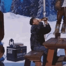 a man is sitting at a picnic table drinking from a bottle .