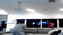 a man and woman are dancing in a living room with a ceiling fan