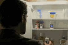 a man looking into a medicine cabinet with a bottle of ibuprofen