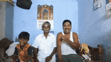 three men are sitting in a room with a calendar on the wall that says ' aadi '
