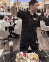 a man in a black shirt is standing in front of a table with a cake on it