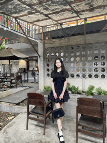 a woman in a black dress is standing in front of a brick wall with holes in it