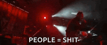 a man is singing into a microphone on a stage in front of a crowd and the words people = shit are visible .