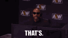 a man wearing sunglasses and a headset is sitting in front of a wall that says aew wrestling
