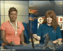 two women standing next to each other with a cat in front of a sign that says gd on it