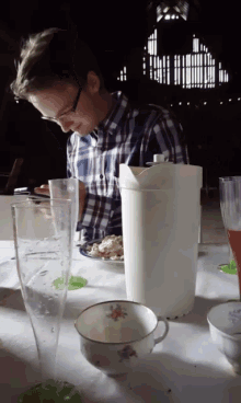 a man in a plaid shirt sits at a table with cups and glasses