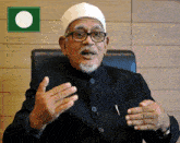 a man wearing glasses and a white hat is sitting in a chair with his hands outstretched
