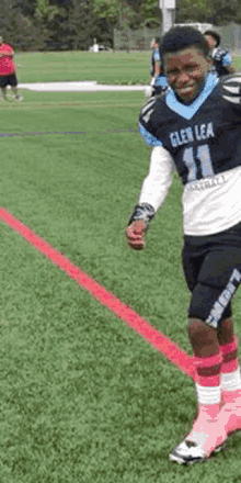 a young boy is standing on a football field wearing a glen lea jersey and pink socks .