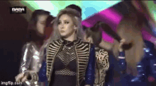 a woman in a black and gold outfit is standing in front of a group of people with the word mama on the bottom