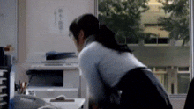 a woman is sitting at a desk in front of a window with chinese writing on it