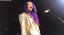 a woman with purple hair is wearing a gold jacket and standing on a stage .