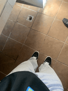 a person standing on a tiled floor with their feet in black sneakers