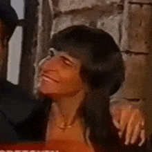 a woman with long hair is smiling while sitting next to a man in a room .