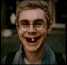 a young man with glasses and a tooth missing is smiling .