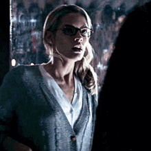 a woman wearing glasses and a sweater is talking to someone