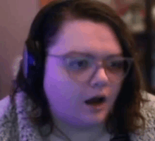 a woman wearing glasses and headphones is looking at the camera with a surprised look on her face .