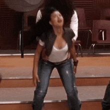 a woman in jeans and a white shirt is standing on a stage with a man standing behind her .