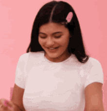 a woman in a white shirt with a pink hair clip is smiling .