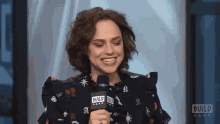 a woman is smiling while talking into a microphone that says build on it