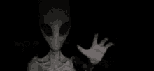a black and white photo of an alien with glowing eyes and a hand in the dark .