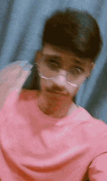a young man wearing glasses and a pink shirt looks at the camera