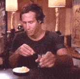 a man is sitting at a table eating a sandwich and drinking a glass of whiskey .