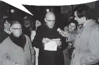 a man in a trench coat is holding a microphone in front of a sign that says ' stazione centrale '