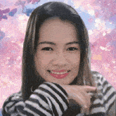 a woman wearing a striped sweater is smiling with a pink background