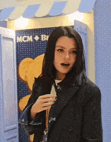 a woman in a black jacket is standing in front of a teddy bear wall .