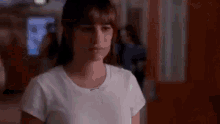 a woman in a white shirt is standing in a hallway and looking at the camera .