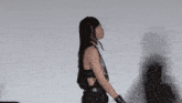 a woman in a black tank top and black pants is standing in front of a white wall