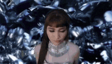 a woman wearing a silver necklace is standing in front of a bunch of diamonds .