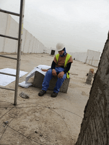 a man in a hard hat sits on a concrete block on a construction site