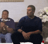 a man in a blue sweater is sitting next to another man in a blue shirt with the words viggle.ai on the bottom right