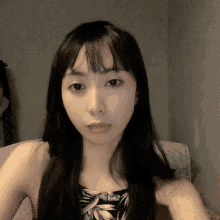 a woman with long black hair is wearing a floral tank top