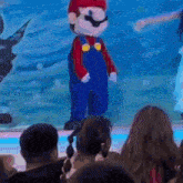 a mario mascot is standing in front of a crowd of people .